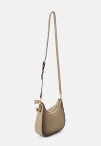 Tan leather shoulder bag with a curved design, adjustable strap, and gold hardware accents. Features a zippered compartment and minimalistic shape.