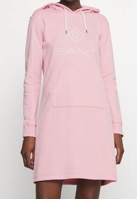 Vestido con capucha rosa hecho de una mezcla de algodón, que presenta un bolsillo tipo canguro, puños acanalados y un logo blanco en el pecho.