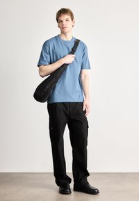 Μπλε βαμβακερό t-shirt, κοντά μανίκια, συνδυασμένο με μαύρο cargo παντελόνι με πλαϊνές τσέπες και μαύρα δερμάτινα παπούτσια. Φοριέται μια μαύρη τσάντα ώμου.