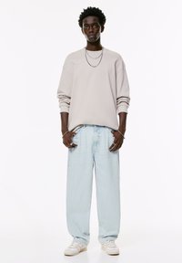 Lichtbeige oversized sweatshirt met brede mouwen, gecombineerd met lichtblauwe jeans met rechte pijpen. Afgemaakt met witte sneakers. Minimalistisch design.