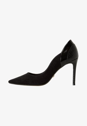 Chaussure à talons hauts noire avec un extérieur en daim, une pointe effilée et des accents en cuir verni noir brillant au talon.