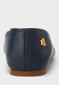 Bailarinas em couro azul-marinho com bico arredondado, detalhe em logotipo dourado no calcanhar e sola em borracha castanha. Textura lisa com costura mínima.