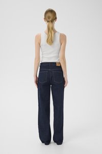 Mørkeblå vide bukser laget av denim, med høy midje, to baklommer og en brun lærmerke på linningen.