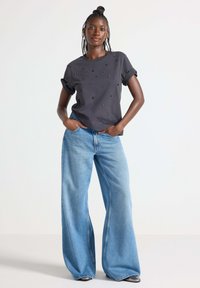 Mørkegrå t-shirt med opdelt ærmer og udsmykkede detaljer, parret med vidde lyseblå jeans med høj talje og løs pasform.