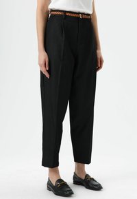 Zwarte, hooggetailleerde broek met plooien, voorzien van een bruine gevlochten riem. Draag ze met zwarte loafers, met strakke lijnen en een op maat gemaakte pasvorm.