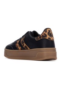 Zapatilla negra con un acento de estampado de leopardo, cuero texturizado y una suela de goma marrón. Presenta cierre con cordones y un diseño de perfil elevado.