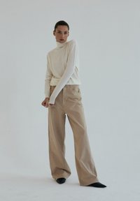 Kremowy sweter z golfem, zestawiony z jasnobeżowymi szerokimi spodniami. Dopasowany krój, ściągacze w prążki oraz minimalistyczny design bez widocznych wzorów.