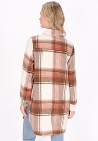 Langærmet flannel skjorte i cremet, orange og brun tern. Har knappedetaljer ved ærmerne og en sideslids for øget bevægelse.