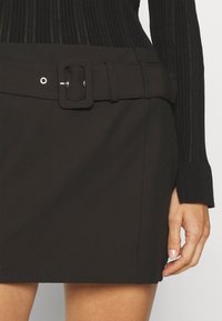 Zwarte mini rok met een brede riem met een rechthoekige gesp en zilveren hardware, gemaakt van een soepele, rekbare stof.