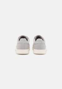 Gray suede sneakers with a textured finish, white rubber soles, and a low-profile design. Features padded collars and subtle branding.