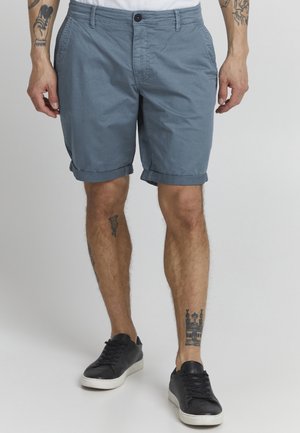 Blå bomuldsshorts med opfoldede kanter, der har sidelommer og en enkelt knaplukning. Bæres med sorte sneakers.