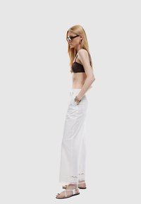 Bruine cropped top, witte wijde broek met kantafwerking, transparante zonnebril en sandalen met bandjes, met een soepele textuur en een nauwsluitende pasvorm.