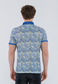 Polo de manga corta en azul y verde con un patrón texturizado. Presenta un cuello y puños de color azul sólido. Diseño ajustado, vista desde la parte posterior.