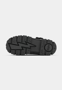 Black rubber shoe sole featuring a zigzag tread pattern, textured surface, and a circular logo. Durable design suitable for various terrains.
