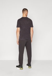 Dunkelgraues T-Shirt mit strukturierter Oberfläche, kombiniert mit dunklen Jogginghosen und schwarzen Sneakers mit grünen Akzenten. Der Hintergrund ist schlicht weiß.