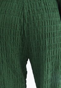 Zelená textura látky ukazuje tkaný vzor s vertikálními liniemi, s mírně zmačkaným povrchem a jemným, lehkým vzhledem.