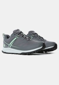 Grå sportskor med texturerad ovandel, ljusgröna detaljer, robust svart sula och en vadderad krage för komfort och stöd.