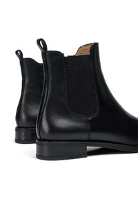 Stivali alla caviglia in pelle nera con pannelli elastici ai lati e un piccolo tacco impilato. Texture liscia e design semplice con accenti minimalisti.