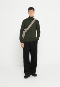 Pulover verde cu guler înalt, cu o croială lejeră, asortat cu pantaloni negri cu croială largă. O geantă gri purtată pe piept completează ținuta. Pantofii negri finalizează look-ul.