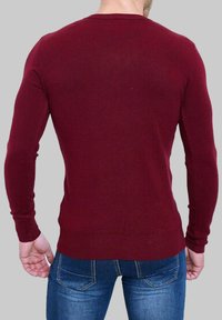 Pull bourgogne à manches longues avec une coupe ajustée, des poignets côtelés et un col rond, associé à un jean bleu clair.