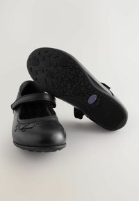 Chaussures Mary Jane en cuir noir avec un bout rond, une sangle ajustable et une semelle en caoutchouc à motif cœur. Présente des accents de couture subtils.
