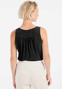 Top in raso nero con scollo rotondo, caratterizzato da un dettaglio plissettato sulla schiena, abbinato a pantaloni beige a vita alta.
