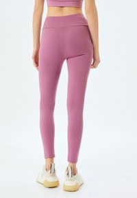Leggings ajustées de couleur rose en tissu extensible avec une taille haute, accompagnées de baskets blanches avec des accents noirs et gris.