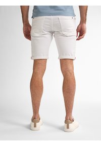 Pantalones cortos de mezclilla blanca con dobladillos enrollados, que presentan dos bolsillos traseros y una textura suave. Combinados con zapatillas beige y blancas.
