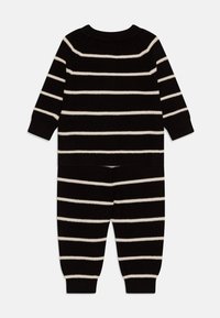 Tutina a righe bianche e nere in maglia con maniche lunghe, scollatura rotonda e polsini e orlo a coste. Caratterizzata da una vestibilità comoda e una consistenza morbida.