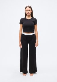 Μαύρο cropped t-shirt με κοντά μανίκια, συνδυασμένο με μαύρο παντελόνι φαρδιάς γραμμής με λευκή ελαστική μέση. Λείο ύφασμα.