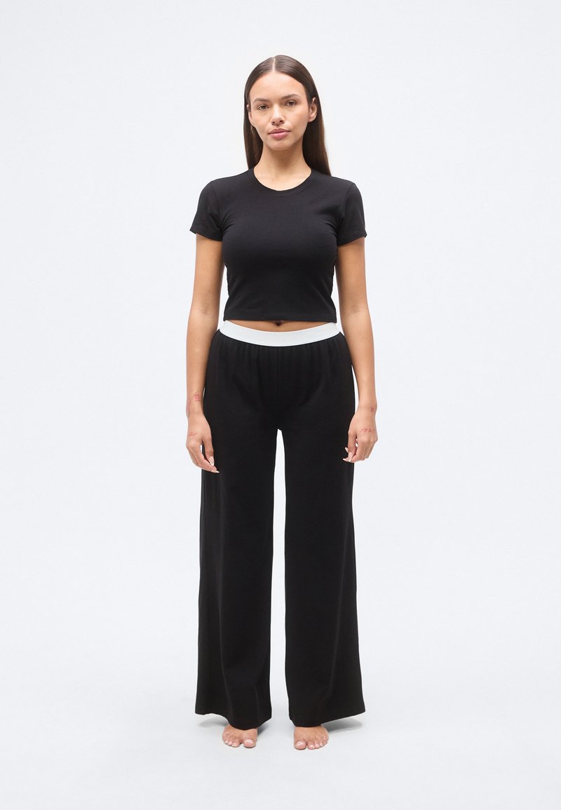 Μαύρο cropped t-shirt με κοντά μανίκια, συνδυασμένο με μαύρο παντελόνι φαρδιάς γραμμής με λευκή ελαστική μέση. Λείο ύφασμα.