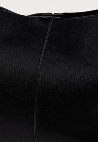 Fekete kézitáska sima, textúrált felülettel. Elegáns, ívelt formája és minimális fém kiegészítői vannak, amelyek tiszta vonalakat és modern megjelenést tükröznek.