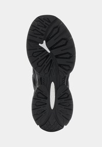 Musta urheilukengän ulkopohja, jossa on kuvioitu kumipinta syvine uurteineen ja keskellä valkoinen korostus.