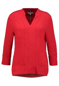 Blusa rossa a maniche lunghe con scollatura a V e dettagli sulle cuciture, caratterizzata da una vestibilità rilassata e un orlo leggermente curvo.