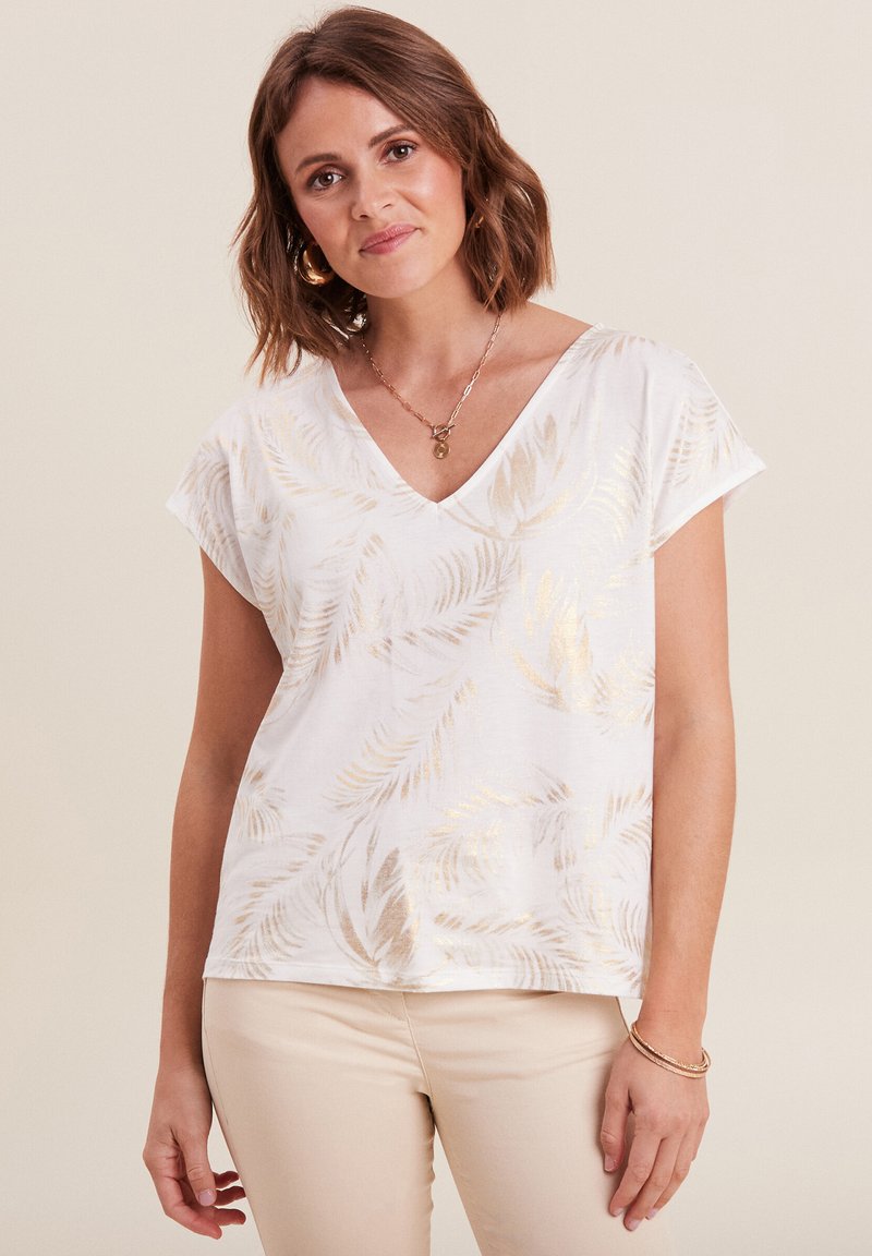 Witte V-hals T-shirt met korte mouwen, met een gouden bladenpatroon. Zachte stof met een ontspannen pasvorm, gecombineerd met beige broeken.