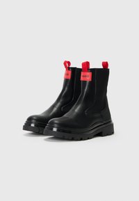 Botas de tornozelo pretas em couro com sola grossa, alças de puxar e marcação vermelha nas laterais. Design elegante com textura suave e construção durável.