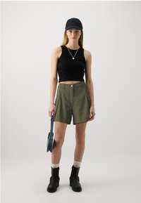 Top scurt negru și pantaloni scurți cargo de culoare verde măslin, cu buzunare frontale și bucle pentru curea. Accesoriile includ o şapcă neagră și o geantă din denim. Bocanci negri.