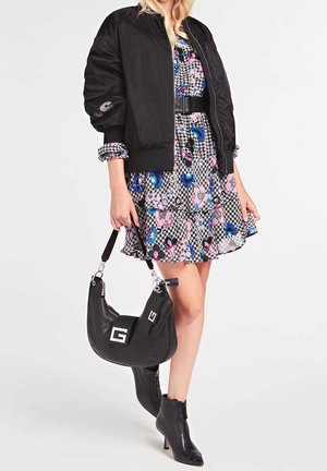 Femme portant une veste bomber noire sur une robe à motif pied-de-poule floral, tenant un sac à main en cuir noir et portant des bottines noires à talons.