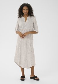 Abito a righe in beige chiaro e marrone, con scollatura a V, maniche corte e un fit rilassato che scende sotto il ginocchio. Completato da sandali neri.