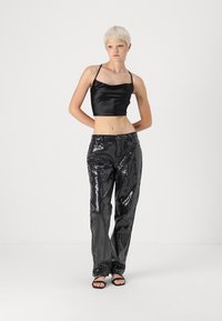 Fekete selyem crop top vékony pántokkal, magas derékú, fényes fekete flitteres nadrággal párosítva. A modellen fekete, nyitott orrú szandál van.