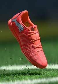 Puma-Fußballschuh in leuchtendem Orange, mit strukturiertem Obermaterial, sechs Schnürlöchern und einem grauen Logo. Entwickelt für Rasenflächen.