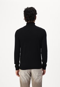 Melna turtlenecka džemperis ar garām piedurknēm, ribotām apakšmalām un aprocēm. Mīksta tekstūra, pieguļoša forma, apvienots ar gaišas krāsas biksēm.