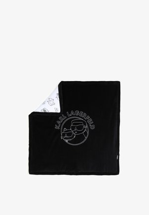 Couverture noire avec dessin en ligne blanche d'une personne et d'un chat portant des lunettes de soleil et le texte "KARL LAGERFELD,", coin replié pour montrer le dessous blanc avec des motifs de croquis similaires.