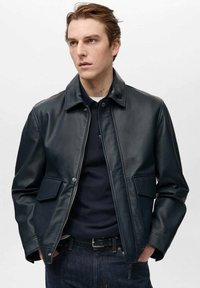 Dunkelblaue Lederjacke mit Kragen-Design, vorderem Reißverschluss, zwei aufgesetzten Taschen und glatter Textur. Über einem dunklen Hemd getragen.