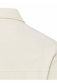 Lysbeige polo-shirt i et struktureret stof, med en klassisk krave og synlige sømme langs skulderen for ekstra detalje.
