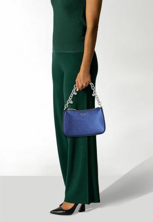 Blaue Ledertasche mit strukturierter Oberfläche, mit einem silbernen Kettenriemen und abgerundeter Form. Kombiniert mit grünen Hosen mit weitem Bein und schwarzen High Heels.