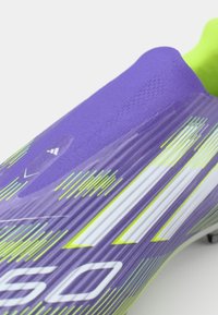 Purple football boot with textured mesh upper, yellow-green accents, and white stripes. Features streamlined design and a flexible collar.