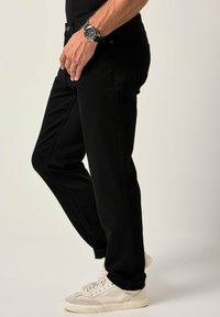 Jeans de mezclilla negra con un corte relajado, que cuentan con bolsillos laterales y una textura suave, combinados con zapatillas blancas y un reloj negro.