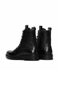 Botas de tobillo de cuero negro con un acabado texturizado, parte delantera con cordones, cremalleras en los laterales y una suela robusta y con taco para mayor agarre.