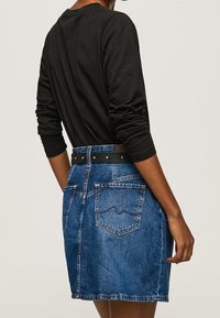 Jeanskjol med bakfickor, ljusblå färg och ett svart bälte. Långärmad svart topp synlig, vilket betonar outfitens avslappnade stil.